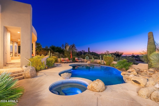 pool at dusk featuring an in ground hot tub and a patio