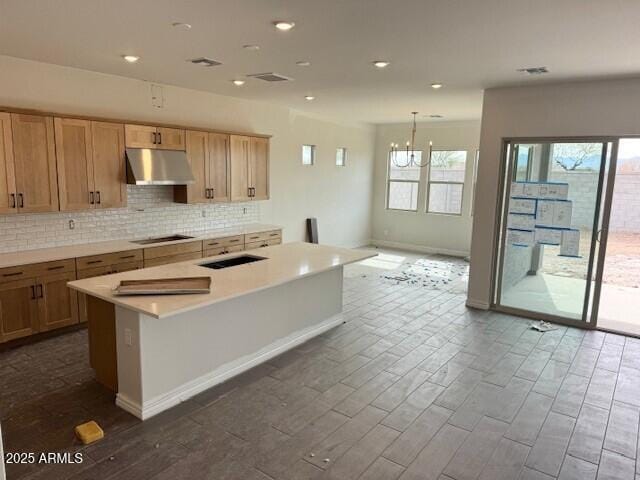 kitchen with black cooktop, dark wood finished floors, decorative backsplash, light countertops, and under cabinet range hood