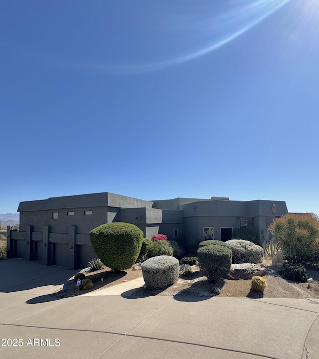 pueblo-style home featuring a garage, concrete driveway, and stucco siding