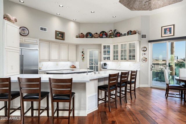 kitchen with visible vents, a high ceiling, glass insert cabinets, a sink, and built in refrigerator