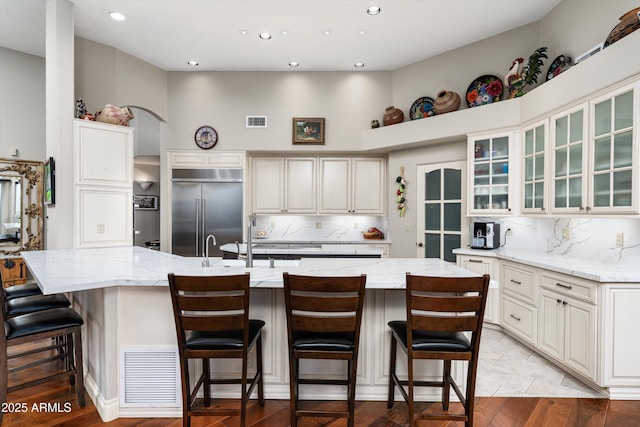 kitchen featuring glass insert cabinets, light stone countertops, visible vents, and stainless steel built in fridge