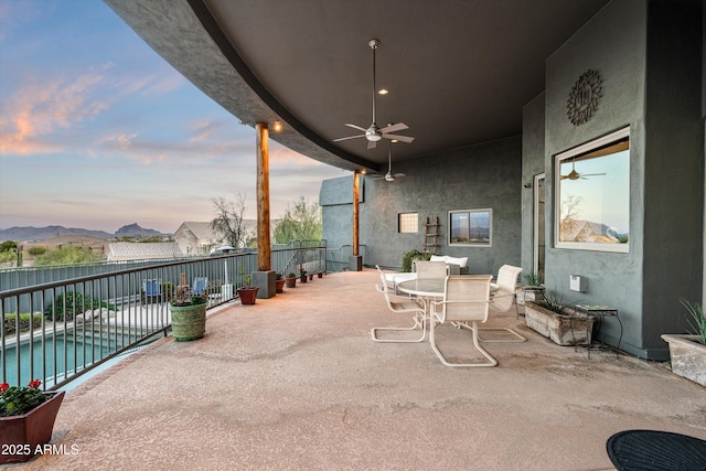 patio terrace at dusk featuring ceiling fan, outdoor dining area, and a fenced in pool