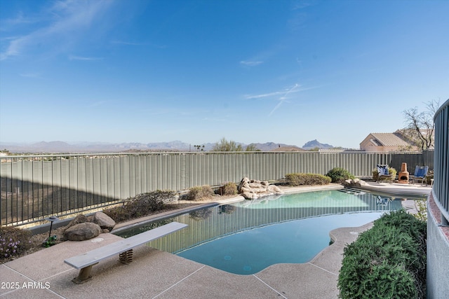 view of pool featuring a fenced in pool, a patio, a fenced backyard, a mountain view, and a diving board