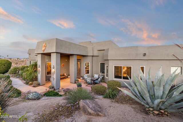 back of property at dusk featuring stucco siding, outdoor lounge area, and a patio