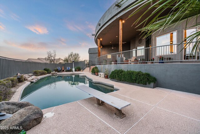 pool at dusk with a patio area, a fenced backyard, a diving board, and a fenced in pool