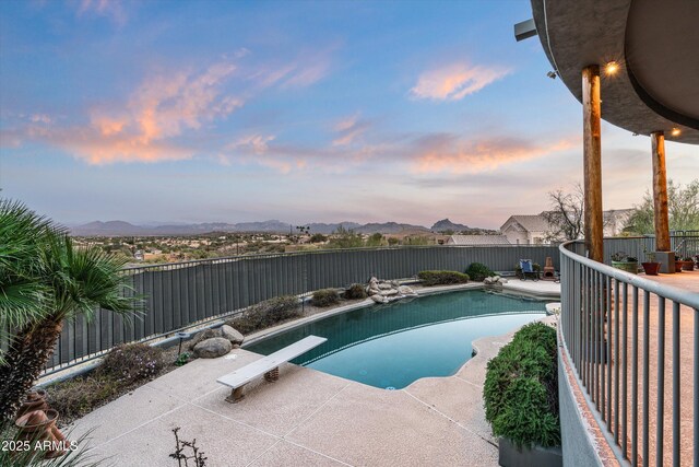 pool at dusk featuring a fenced in pool, a fenced backyard, a patio, and a diving board