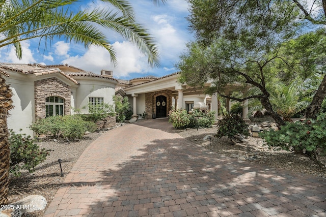 mediterranean / spanish-style home featuring stone siding, stucco siding, a tiled roof, and decorative driveway