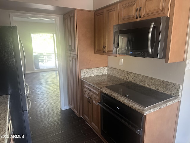 kitchen with dark hardwood / wood-style floors, light stone counters, and black appliances