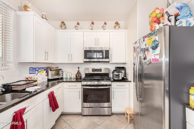 kitchen with white cabinetry, stainless steel appliances, backsplash, dark stone counters, and light tile patterned floors