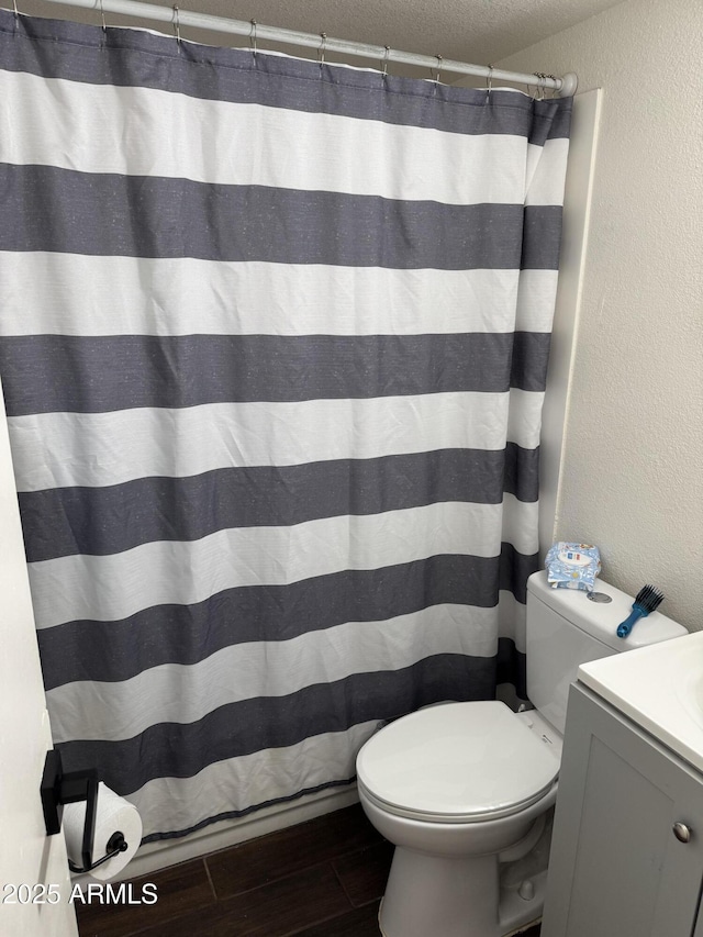 full bath with a textured ceiling, a textured wall, toilet, wood finished floors, and vanity