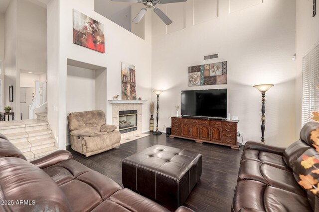 6971 W El Cortez Pl, Peoria, AZ 85383 - living room featuring a towering ceiling, dark wood-style flooring, a ceiling fan, a tile fireplace, and stairway