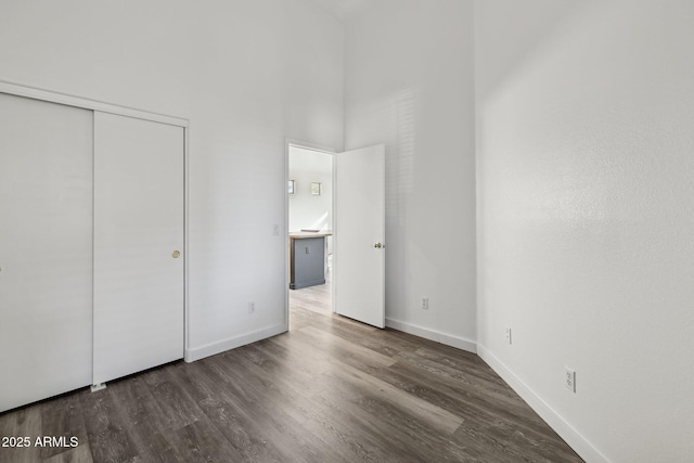 unfurnished bedroom featuring wood finished floors, a towering ceiling, a closet, and baseboards