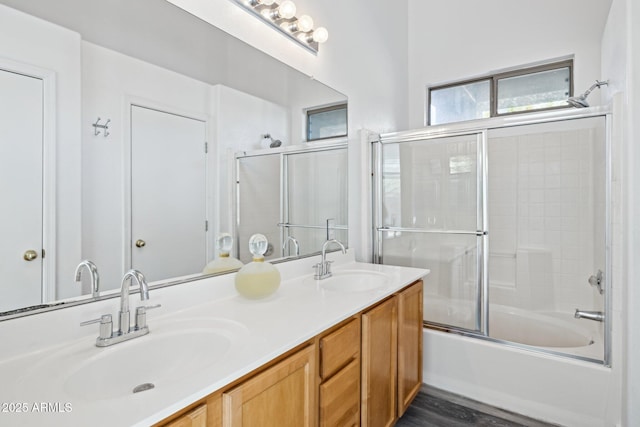 full bath with combined bath / shower with glass door, double vanity, a sink, and wood finished floors