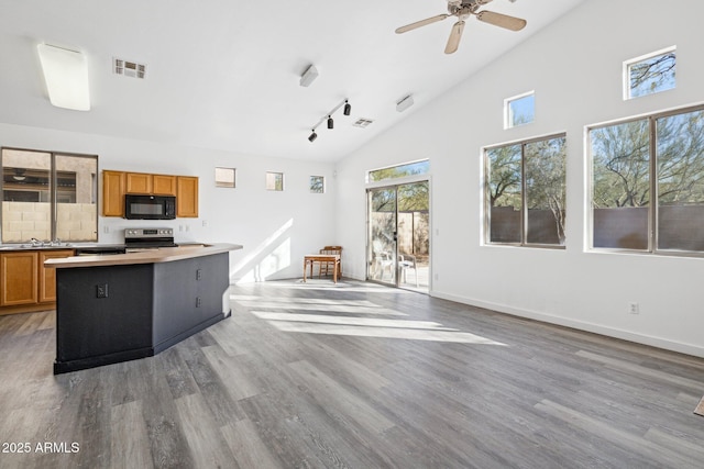 kitchen with brown cabinets, wood finished floors, a kitchen island, and black microwave