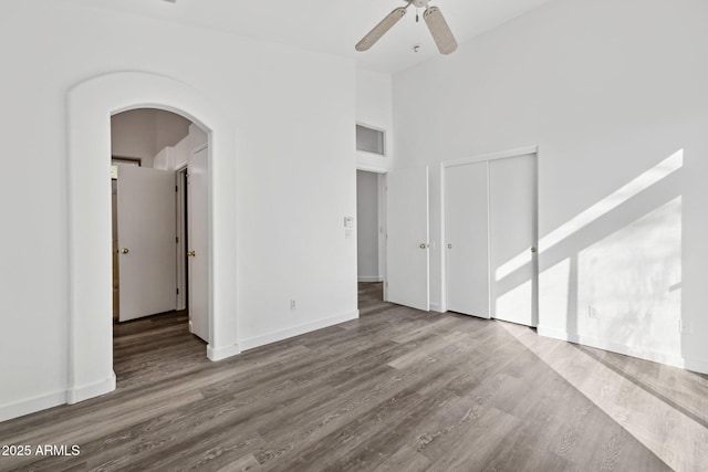 unfurnished room with baseboards, arched walkways, ceiling fan, wood finished floors, and high vaulted ceiling