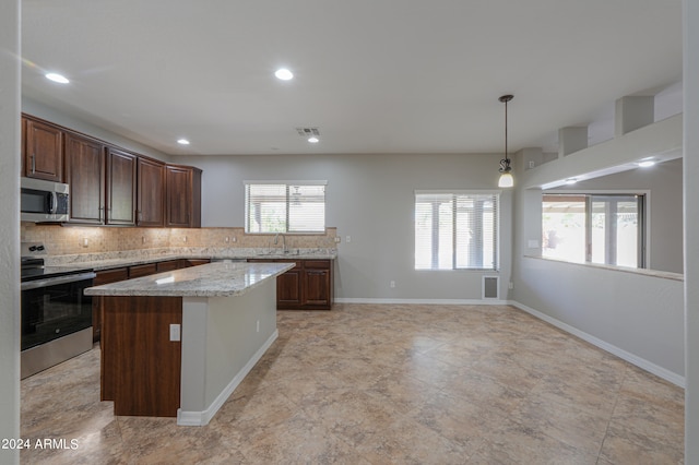 kitchen with light stone counters, sink, backsplash, appliances with stainless steel finishes, and a center island