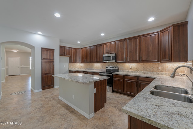 kitchen with light stone counters, sink, stainless steel appliances, a center island, and decorative backsplash