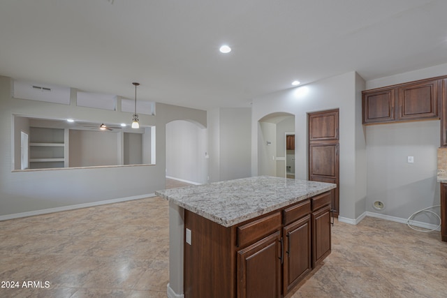 kitchen with light stone countertops, built in shelves, decorative light fixtures, and a center island