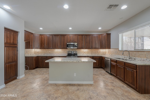 kitchen featuring a kitchen island, sink, stainless steel appliances, light stone countertops, and backsplash