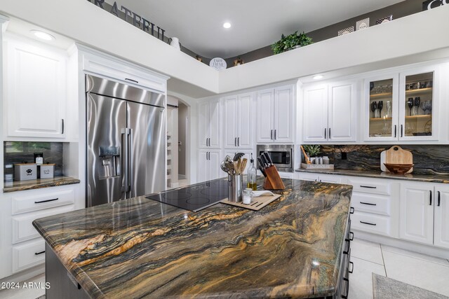 kitchen featuring dark stone countertops, built in appliances, light tile patterned floors, a kitchen island, and white cabinets