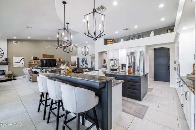 kitchen featuring white cabinets, dark stone countertops, decorative light fixtures, a large island with sink, and built in fridge