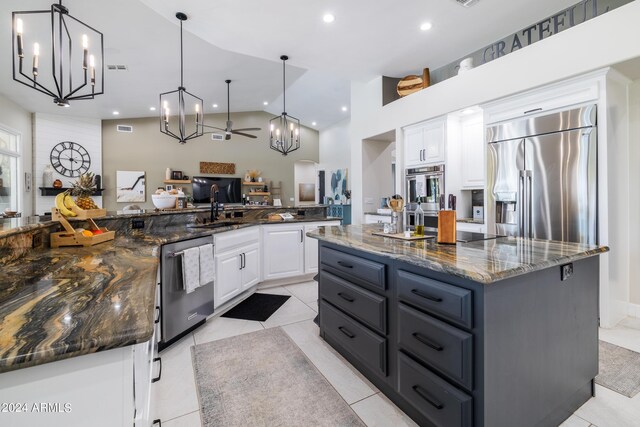 kitchen featuring dark stone countertops, ceiling fan with notable chandelier, white cabinetry, appliances with stainless steel finishes, and a large island