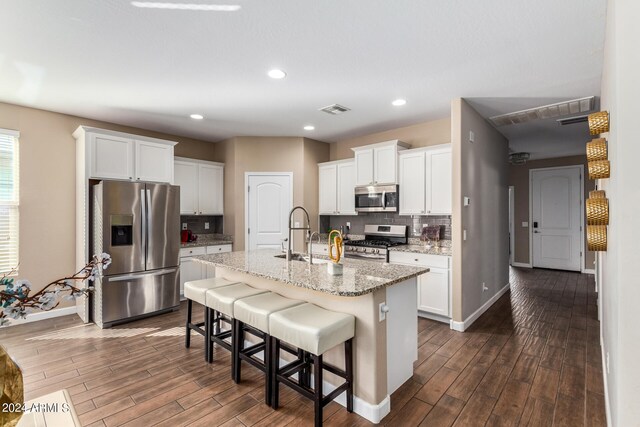 kitchen with a center island with sink, dark wood-type flooring, appliances with stainless steel finishes, and white cabinetry