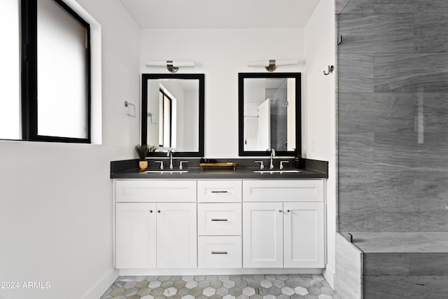 full bathroom featuring tiled shower, double vanity, baseboards, and a sink