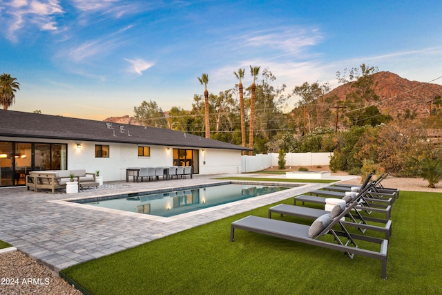 pool at dusk featuring outdoor lounge area, a yard, a patio area, and a fenced backyard