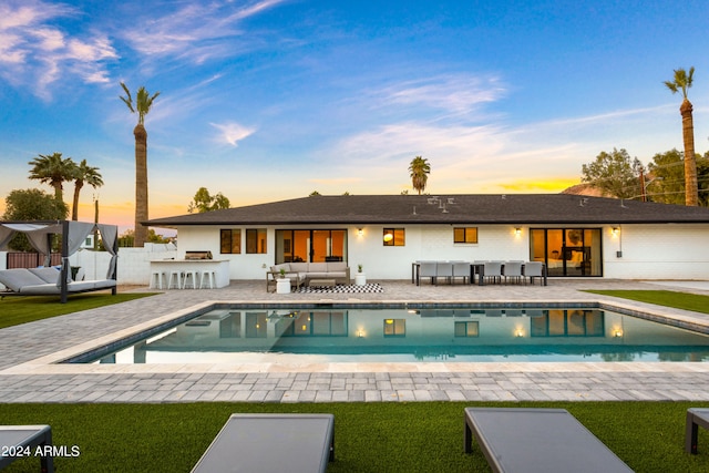 back house at dusk featuring outdoor lounge area, a patio, a yard, and exterior kitchen