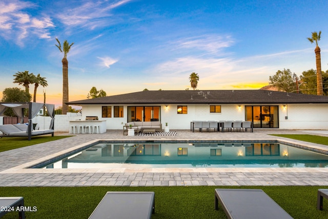 back of house at dusk featuring a patio area, an outdoor living space, outdoor dry bar, and an outdoor pool