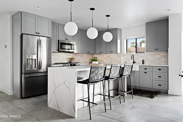 kitchen with light stone countertops, a breakfast bar, gray cabinets, stainless steel appliances, and decorative backsplash