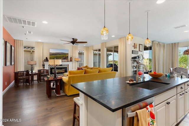 kitchen featuring decorative light fixtures, dishwasher, sink, dark wood-type flooring, and a center island with sink