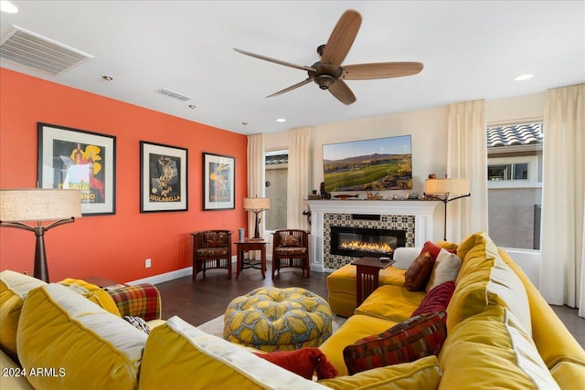 living room with a tiled fireplace, dark wood-type flooring, and ceiling fan