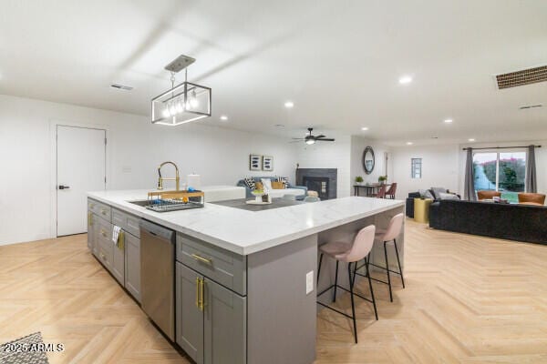 kitchen featuring gray cabinetry, sink, dishwasher, light parquet flooring, and an island with sink