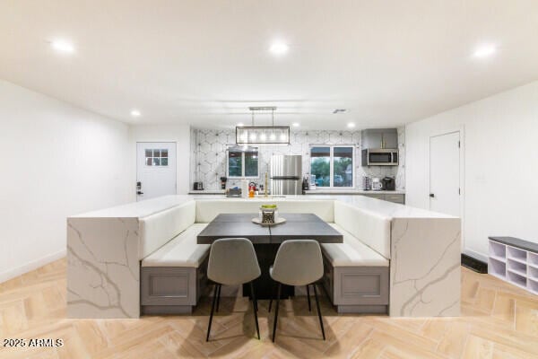 kitchen with light parquet floors, hanging light fixtures, decorative backsplash, appliances with stainless steel finishes, and kitchen peninsula