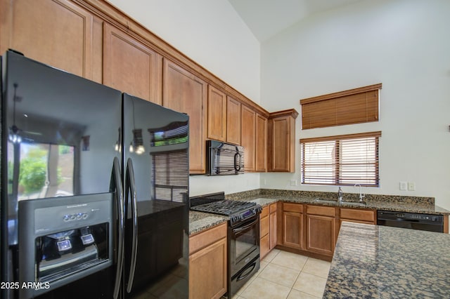 kitchen with brown cabinets, a sink, light tile patterned floors, black appliances, and dark stone counters