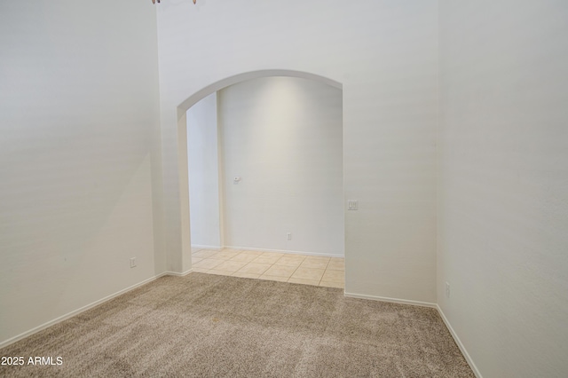 empty room featuring arched walkways, baseboards, light carpet, and light tile patterned floors
