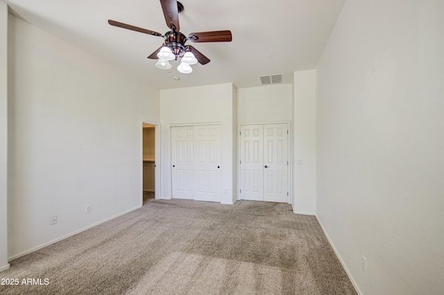 unfurnished bedroom featuring two closets, baseboards, visible vents, and carpet