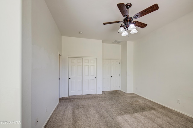 unfurnished bedroom with two closets, carpet flooring, visible vents, and baseboards