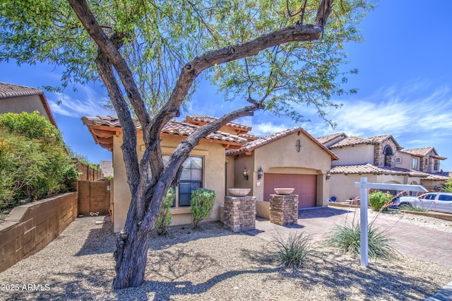 mediterranean / spanish-style home with fence, an attached garage, decorative driveway, and stucco siding