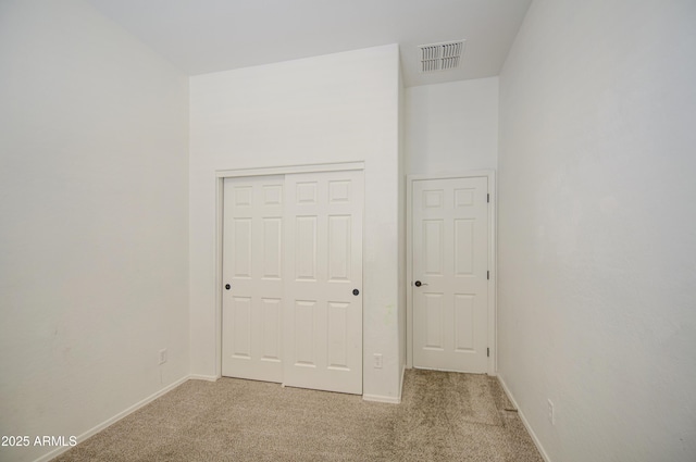 unfurnished bedroom featuring light colored carpet, baseboards, visible vents, and a closet
