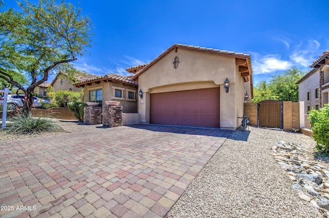 mediterranean / spanish house with decorative driveway, stucco siding, a gate, a tiled roof, and an attached garage