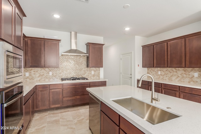 kitchen featuring wall chimney range hood, sink, decorative backsplash, light stone countertops, and appliances with stainless steel finishes