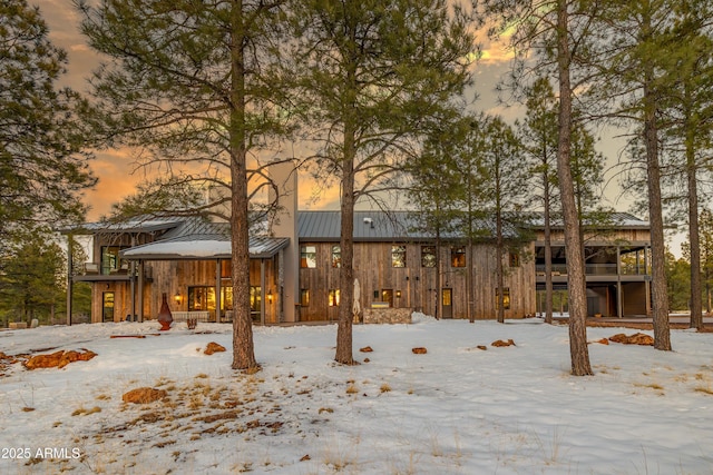 snow covered back of property with metal roof, stone siding, and a standing seam roof