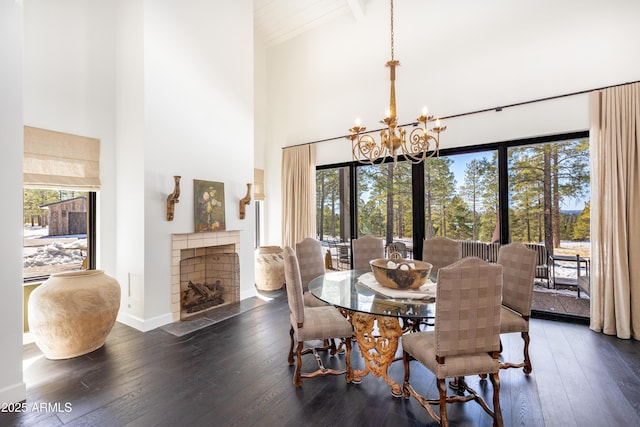 dining space featuring baseboards, a chandelier, a fireplace with flush hearth, a high ceiling, and wood-type flooring