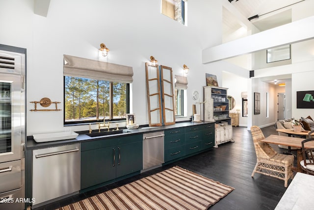 kitchen with stainless steel dishwasher, dark countertops, a towering ceiling, and a sink