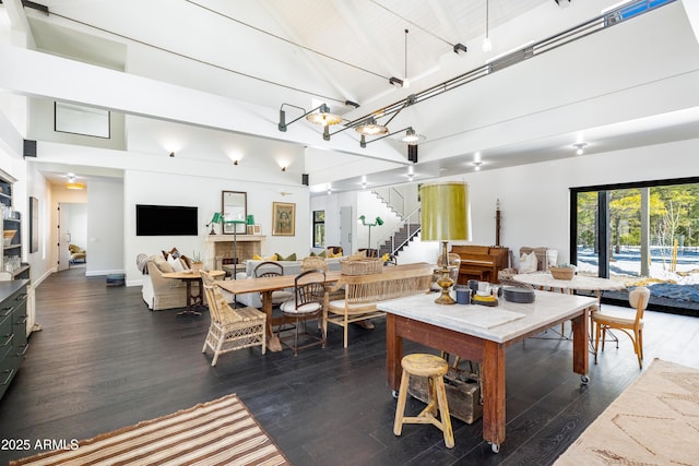 dining space with dark wood-style floors, stairway, a fireplace, and high vaulted ceiling