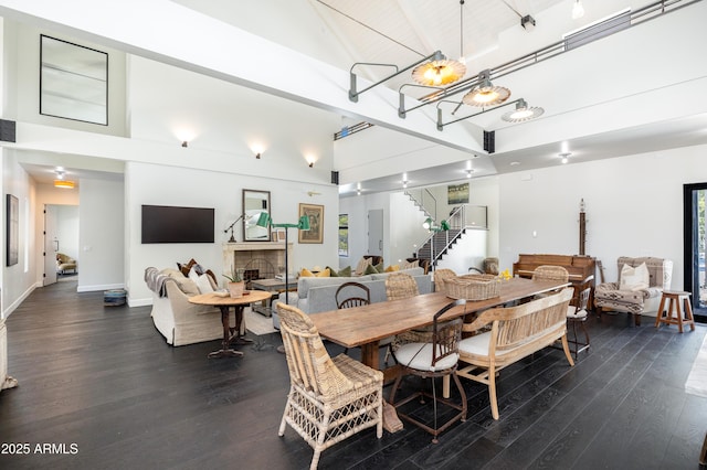 dining area with stairway, a fireplace, dark wood-style flooring, and high vaulted ceiling