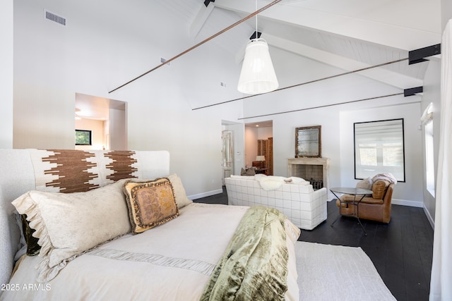 bedroom with visible vents, beamed ceiling, a tiled fireplace, wood finished floors, and baseboards